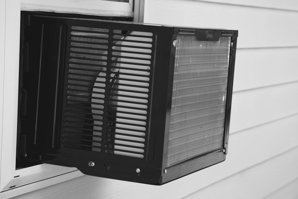 black ac window unit sticking out of a window of a house with white paneling